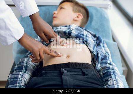 Child physical examination concept. Unrecognizable African American doctor performing manual palpation. Female pediatrician or health care practitioner examines little boy abdomen Stock Photo