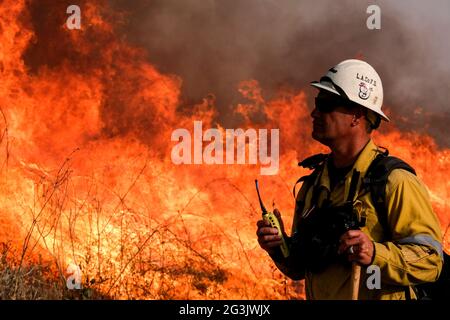 Irwindale, California, USA. 15th June, 2021. A firefighter watches as a brush fire burning in the Santa Fe Dam Recreation Area. Credit: Ringo Chiu/ZUMA Wire/Alamy Live News