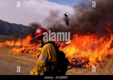 Irwindale, California, USA. 15th June, 2021. A firefighter walks away as a helicopter drops water at a brush fire burning in the Santa Fe Dam Recreation Area. Credit: Ringo Chiu/ZUMA Wire/Alamy Live News
