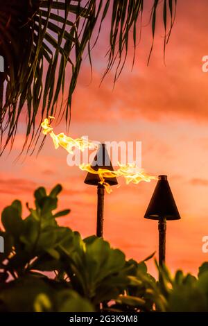 Hawaii luau party Maui fire tiki torches with flames burning against sunset sky clouds at night. Hawaiian culture travel background. Stock Photo