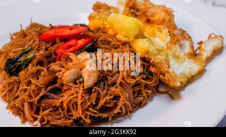 Stir fried vermicelli or Bihun goreng, Malaysian style spicy stir fried vermicelli with fried egg and chicken chunks. Top with red chilli as garnishin Stock Photo