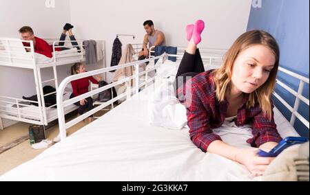Girl with phone lying on bed in hostel Stock Photo