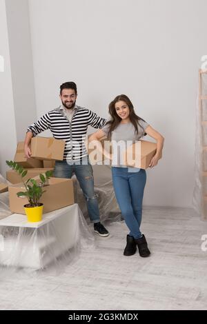 Excited young couple moving home standing close together with cardboard cartons in their hands. Stock Photo