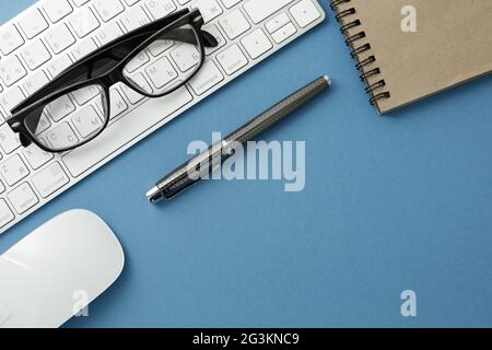 Glasses keyboard notepad mouse and pen on blue background Stock Photo