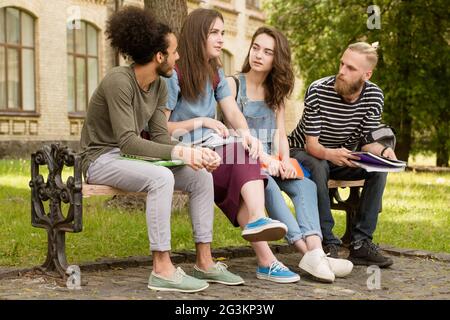 Students sitting on bench telling stories. Stock Photo