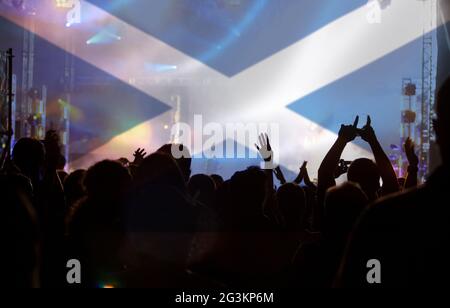 Soccer fans supporting Scotland - crowd celebrating in stadium with raised hands against Scotland flag Stock Photo