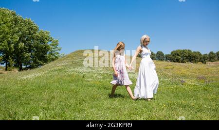 Sunny day, mother and little girl walking in the field. Stock Photo