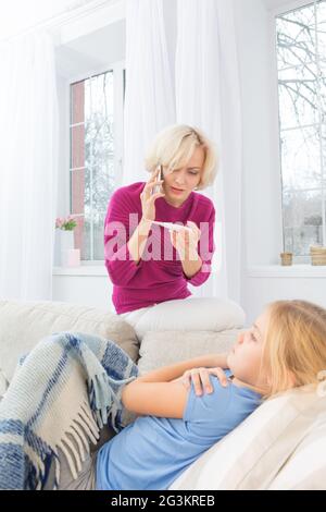 Worried mom calling doctor holding thermometer in hand. Stock Photo