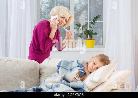 Young worried mom calling doctor measuring temperature of her daughter. Stock Photo