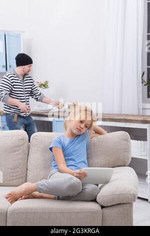 Sick little child sitting on sofa watching cartoons on tablet. Stock Photo