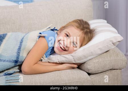 Little girl, sick lying on sofa and smiling. Stock Photo