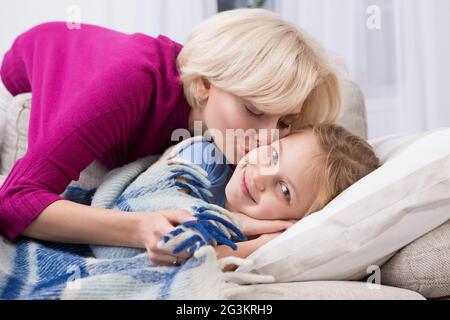 Sick little girl staying at home, mom kissing her. Stock Photo