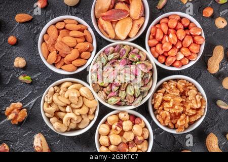 Nuts in bowls and scattered, top shot on a black background. Pistachios, peanuts, walnuts and other vibrant nuts Stock Photo