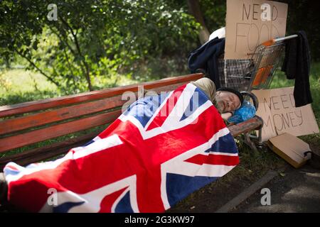 Homeless man sleeping on bench, covering with flag of Great Britain. Stock Photo