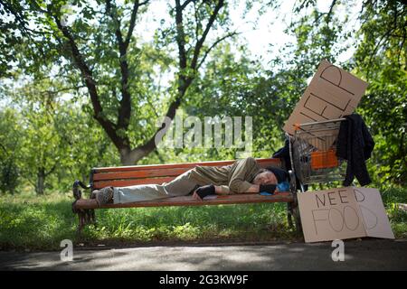 Homeless old man on the bench in city park. Stock Photo