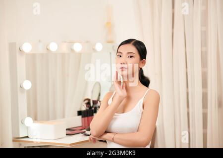 Female Skin Care. Young asian woman touching her face and looking to mirror Stock Photo