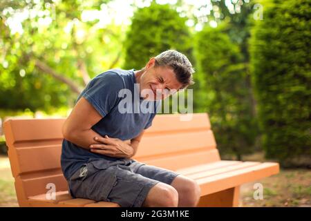 Man with stomach pain sitting on the bench in the park. Healthcare and medicine concept Stock Photo