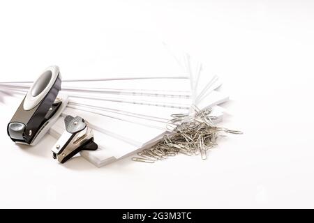 Photograph on a white background of some fan-shaped sheets of paper, a stapler, a staple extractor and some paper clips.The photo has free space to pu Stock Photo