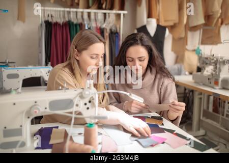 Close up of female fashion stylist and customer holding color samples of fabrics choosing design for new dress, copy space Stock Photo