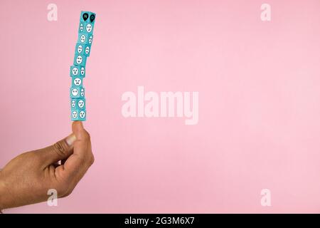 hand holding a stack of wooden blocks in balance with shapes of a different faces on a pink background Stock Photo