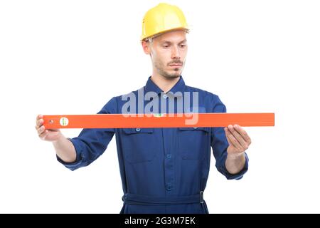 Portrait of successful handsome young adult Caucasian construction engineer wearing uniform with hardhat measuring level of something Stock Photo