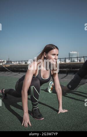 Sportive young woman doing streching exercises on the roof. Stock Photo