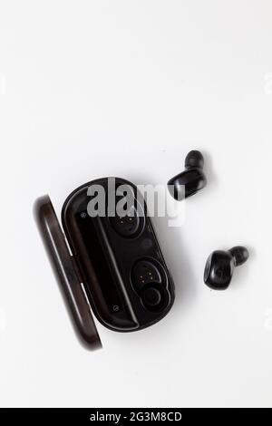 Black wireless bluetooth headphones and their charging base placed on a white background. The headphones are out of the charger and have the silicone Stock Photo