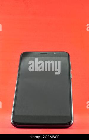 Smartphone turned off and semi-upright, black, placed on a red background. Stock Photo
