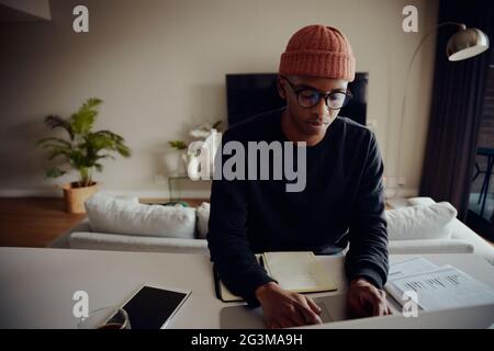 African American male working from home and browsing on his laptop. African American man writing notes and typing on his laptop. High quality photo Stock Photo