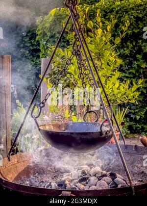Outdoor cooking using charcoal in fire bowl with tripod and pot hanging from chains Stock Photo