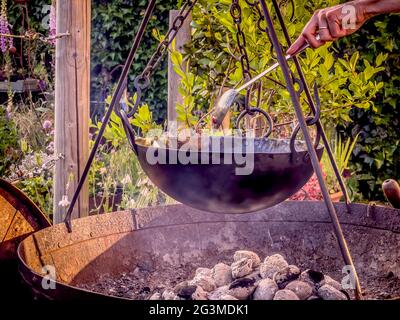 Outdoor cooking using charcoal in fire bowl with tripod and pot hanging from chains Stock Photo