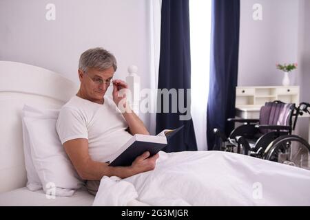 Disabled man reading in bed. Stock Photo