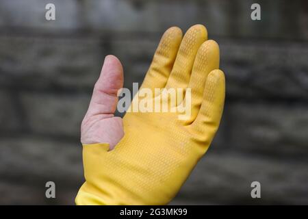 Man is doing chores around the house with yellow and blue gloves. Used broken yellow grove showing off the thumb. Taking the trash out from the bin. T Stock Photo