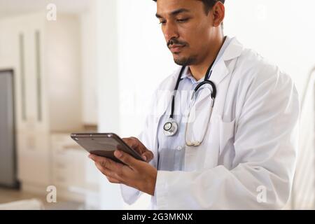 Hispanic male doctor in lab coat concentrating using digital tablet Stock Photo