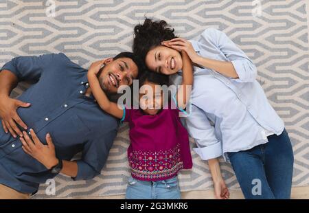 Portrait of smiling hispanic mother, father and daughter lying floor embracing Stock Photo