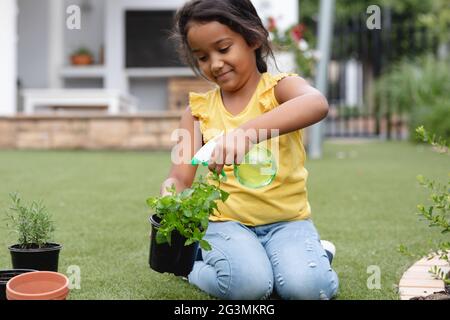 Smiling hispanic girl gardening, kneeling and watering plant in pot Stock Photo