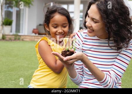 Smiling hispanic mother and daughter gardening, mother holding seedling in hand Stock Photo