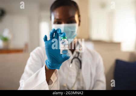 African american female doctor in face mask and gloves holding vial of covid 19 vaccine Stock Photo