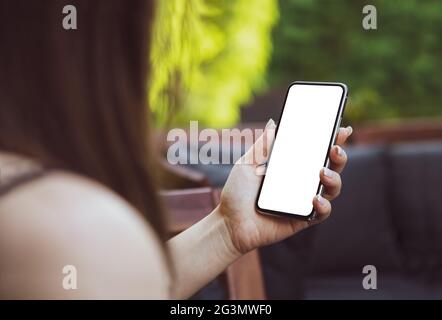 Girl using smartphone blank screen frameless modern design while lying on the sofa in garden Stock Photo