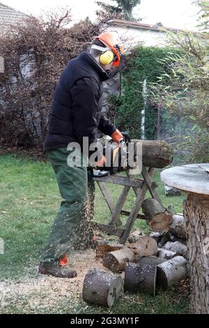 "28.11.2020, Neuenhagen, Brandenburg, Germany - Young man saws up a tree trunk with a circular saw in an allotment garden. 00S201128D399CAROEX.JPG [MO Stock Photo