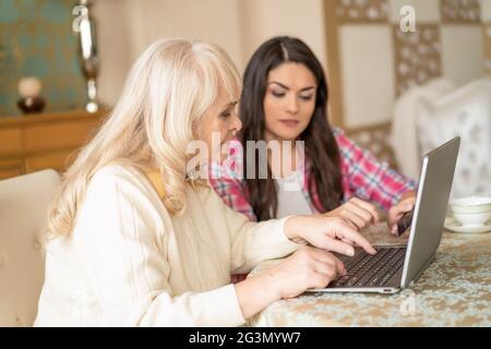 Young daughter teaches senior mother how to type on a laptop Stock Photo