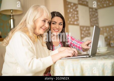 Young daughter teaches senior mother how to use a laptop by pointing on the screen Stock Photo