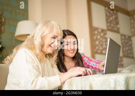 Young daughter teaches senior mother how to use a laptop by pointing on the screen Stock Photo