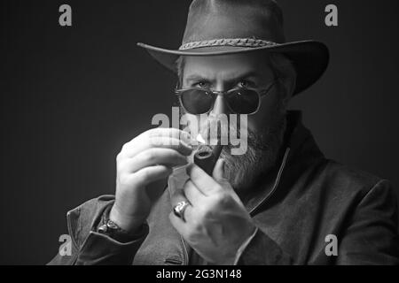 Menacing vintage cowboy standing with pipe for smoking. Studio shot ...