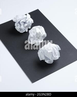 Crumpled paper balls on a black sheet of paper on a white background Stock Photo