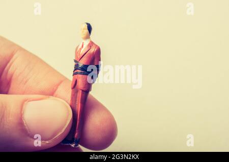 Hand holding tiny figurine of man model tied in rope Stock Photo