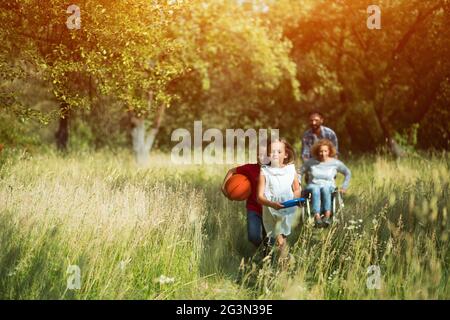 Children ran and laugh while their mother on wheelchair and father are running after them Stock Photo