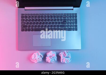 Laptop, crumpled paper balls close up. Neon light. Modern business concept. Stock Photo