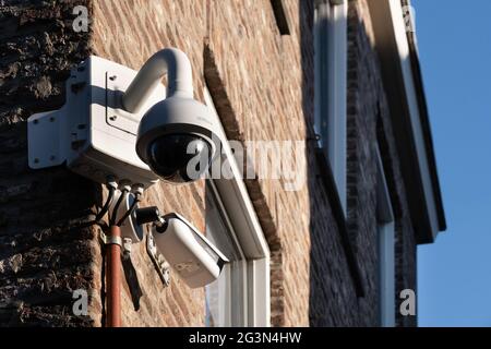 Two different types of surveillance or security CCTV cameras on a brick wall of a shop in the center of Maastricht, the Netherlands. Blue sky Stock Photo
