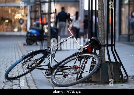 Black bicycle is half on the ground and half against a tree in a shopping street, parked carelessly or overturned. Fallen bicycle on the street Stock Photo